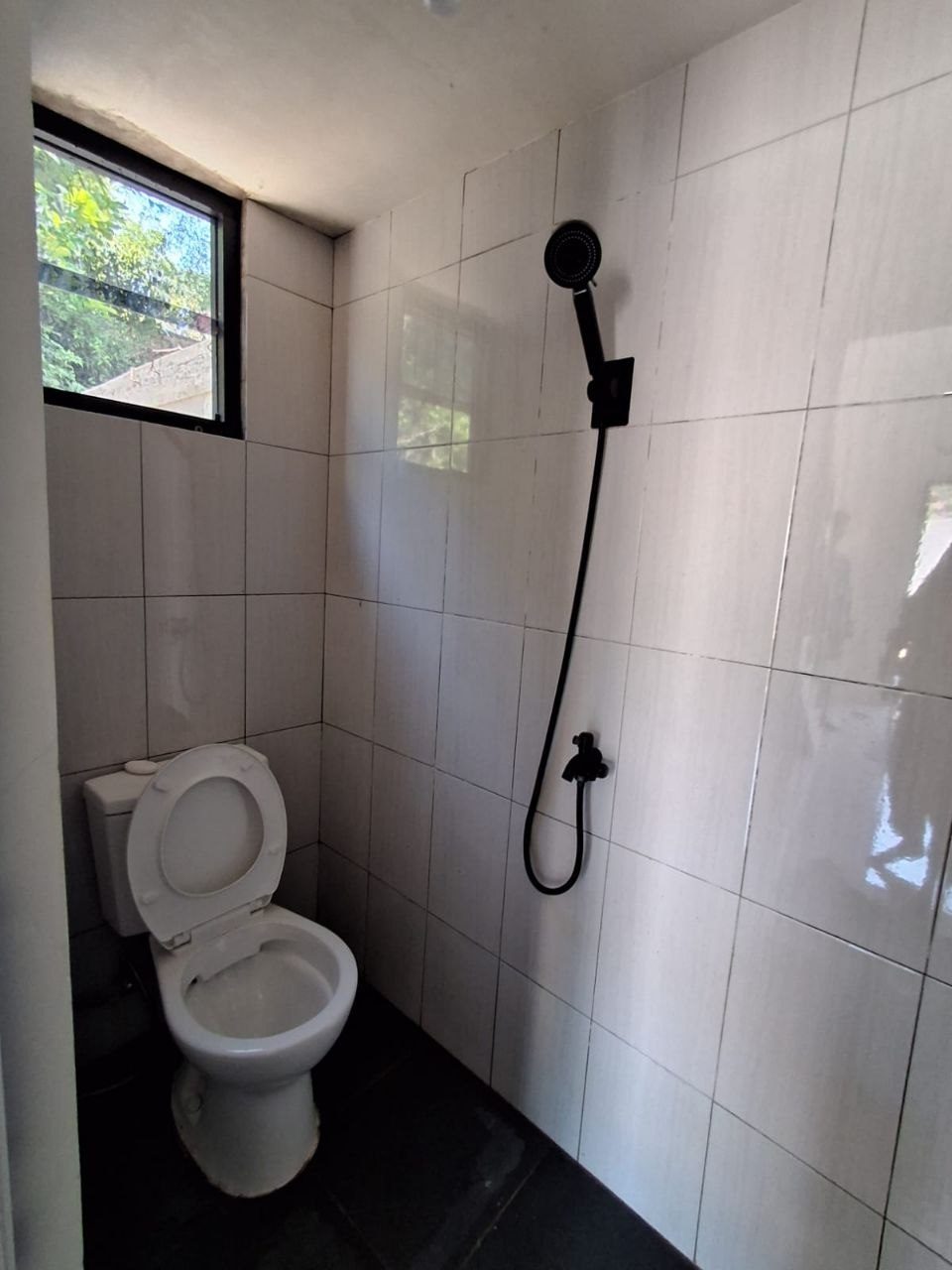 Kamar mandi rumah baru Megah Residence 2 Gunungpati Semarang, dinding keramik putih, shower set hitam matte, kloset duduk, ventilasi jendela