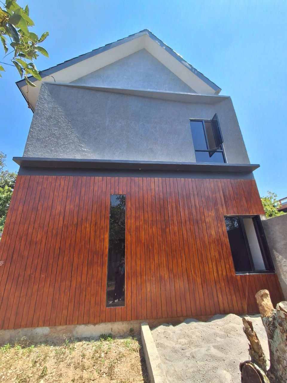 Tampak elevasi belakang rumah Megah Residence 2 Gunungpati Semarang, dinding kayu kombinasi abu-abu, jendela vertikal tinggi, desain modern tropis