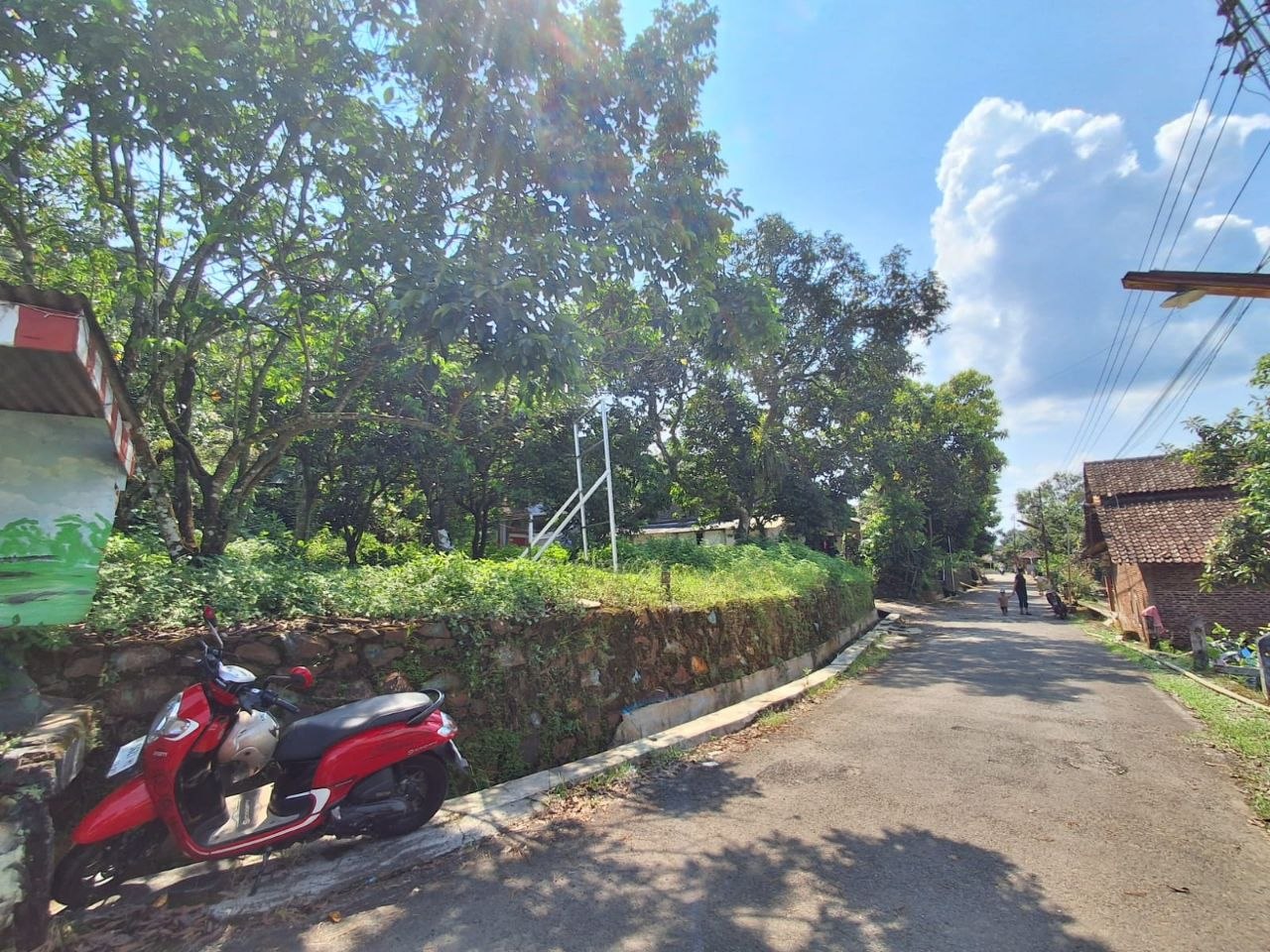 Akses jalan utama kampung Sabrangan, Plalangan, Gunungpati, dengan motor dan pagar batu warna-warni.