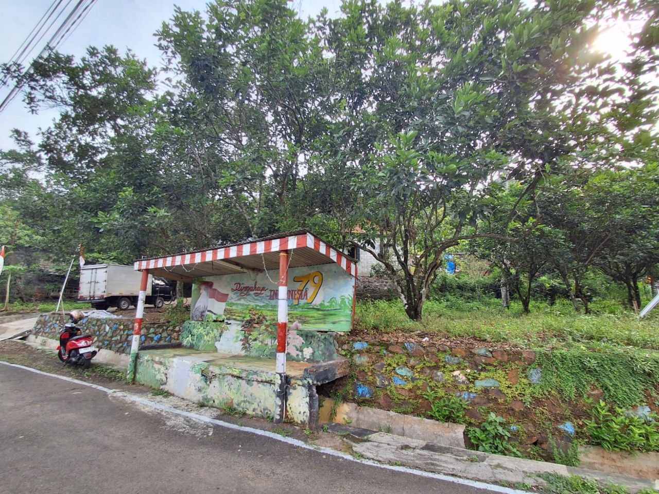 Halte RW 03 Sabrangan dengan lukisan Pesona Indonesia, pagar batu warna-warni, motor warga di depan.
